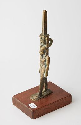 une statue égyptienne représentant un homme tenant une épée, posée sur un socle en bois