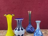 quatre vases de couleurs différentes posés sur une table, avec un mur rouge en arrière-plan