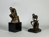deux sculptures en bronze représentant un homme et une femme assis sur des cubes