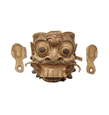 un masque en bois devant lequel se trouvent deux cuillères en bois