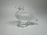un canard en verre posé sur un socle transparent