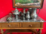 a painting on the wall above a table with silver pots and teapots on it