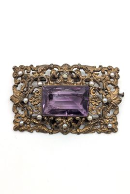 un gros plan sur une broche composée d'une pierre violette et d'une perle