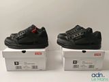 two pairs of black sneakers sitting on top of boxes on a white surface