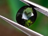 un gros plan d'un diamant vert tenu par une pince