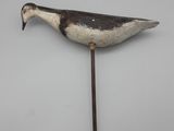 une image représentant un canard en bois fixé sur un bâton, posé sur une surface blanche