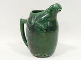 a green pitcher with a frog on it on a white surface