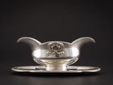 une saucière ancienne en argent posée sur un plateau, sur fond noir