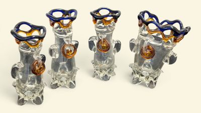 four glass vases with scissors in them on a white surface