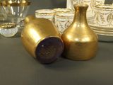 a gold vase and cups on a table next to each other