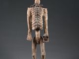 une figurine en bois représentant un squelette debout sur une surface grise