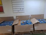 Plusieurs cartons de sodas sont empilés sur des palettes dans une pièce