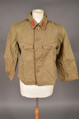 une vieille veste militaire posée sur un mannequin, devant un fond gris