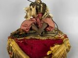 an old doll sitting on a red cushion with a pipe in its mouth