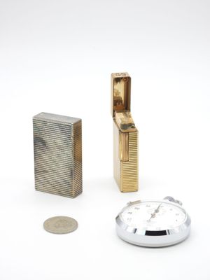 un briquet, une horloge et une pièce de monnaie posés sur une surface blanche