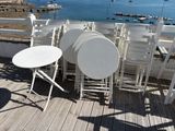 tables and chairs on a deck overlooking a body of water with boats in the distance
