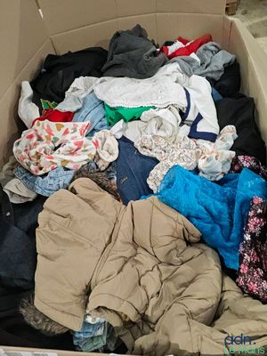 un carton rempli de vêtements et des vêtements par terre