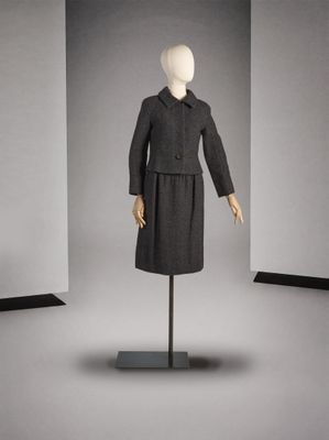 un mannequin vêtu d'un manteau et d'une jupe noirs, posé sur un socle