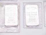 three silver bars are in plastic bags on a white surface