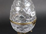 an egg shaped glass box with a gold trim around the base
