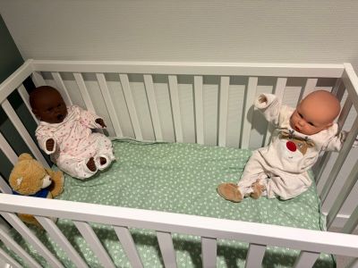 two baby dolls sitting in a crib next to each other