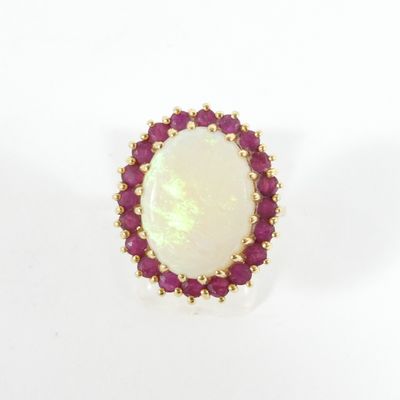 un gros plan d'une bague en oplite blanche et rubis posée sur une surface blanche