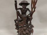 carved wooden figurine of a man sitting on a tree stump with a hat and cane