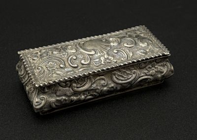 une boîte ancienne en argent posée sur une surface noire, avec un fond noir