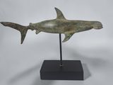 a bronze shark sculpture on a black stand on a white background