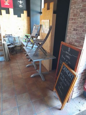 Des tables et des chaises sont alignées à l'extérieur d'un restaurant, devant un panneau écrit à la craie.