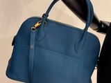 blue leather handbag hanging from a black pole on a white wall