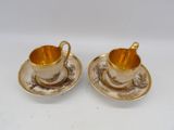 two cups and saucers with gold rims on a white surface