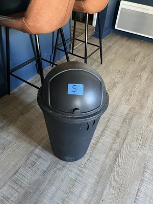 une poubelle noire posée par terre à côté d'une chaise marron