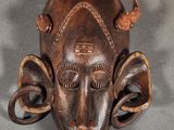 an image of a wooden mask with horns on a gray surface