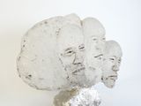 a sculpture of three faces on a rock on a white surface