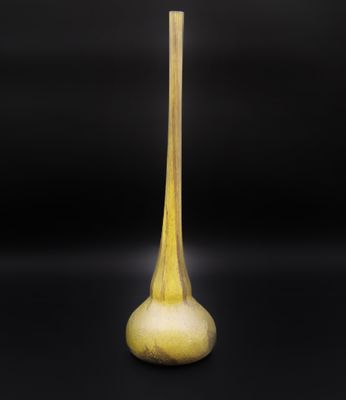 un vase jaune à long pied posé sur une surface noire