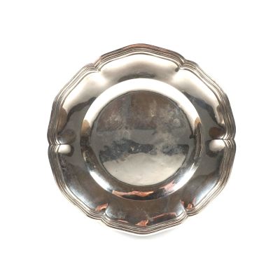 une assiette en argent sur fond blanc, dans laquelle on voit un reflet