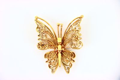 broche en forme de papillon doré aux ailes en filigrane sur fond blanc