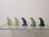 a glass shelf that has five different colored glass frogs on it