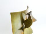 a metal sculpture of a bird that is on top of a piece of paper