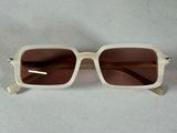lunettes de soleil beiges aux verres marron, posées sur une surface blanche