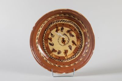 une assiette marron et blanche posée sur un socle, sur laquelle se trouve une horloge