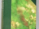 an old book with a green cover sitting on top of a white table