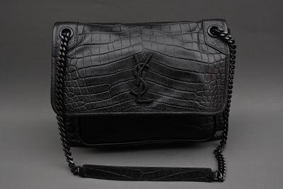 le sac à main noir est posé sur une surface grise, entouré d'une chaîne