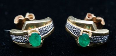 une paire de boucles d'oreilles en émeraude et diamant posées sur un fond noir