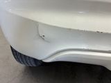 the rear end of a white car with a dent in it