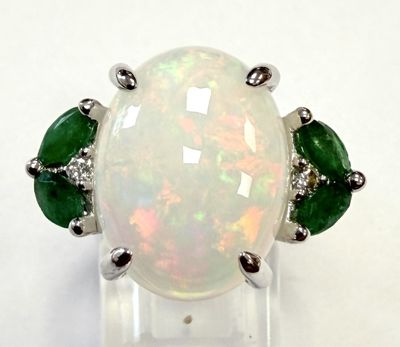 une bague en oplite et émeraude posée sur un socle en acrylique transparent