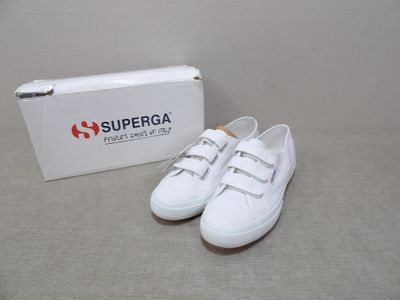 des baskets Superga blanches avec une boîte posée par terre