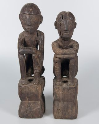 pair of carved wooden figures of two men sitting on stools