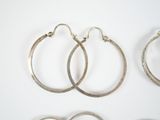 three pairs of silver hoop earrings sitting on top of a white surface